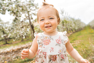 Adorable little smiling baby girl playing in a blooming apple garden