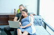 © narong - Pregnant woman using laptop and stay on sofa with husband in living room with day light.