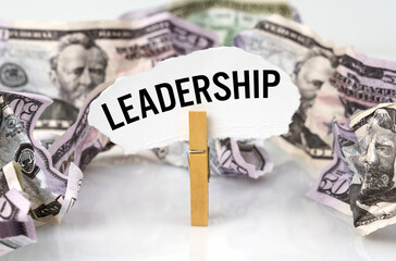 There are dollars on the table and there is a clothespin with paper on which it is written - LEADERSHIP