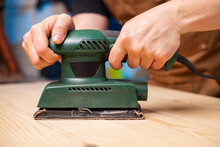 Closeup Of Carpenter Sanding Wooden Planks With Electrical Sanding Machine. A Carpenter Grinds Wood With Sander Machine