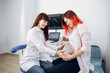 © sofiko14 - Young professional female Caucasian doctor touches the belly of a pregnant woman during regular check up at modern obstetrics center. Pretty joyful red haired pregnant woman talking with doctor