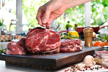 Poster - Hand sprinkling salt on fresh raw beef meat on a cutting board in the kitchen