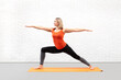 Caucasian athletic woman in orange tank top practice yoga indoor in loft fitness studio. Warrior pose II, full length.