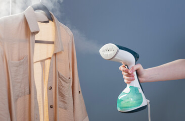 female hand with steamer and shirt on blue background