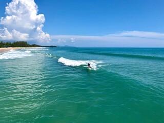 A young man surfer riding waves at Natai beach in Phang Nga, Thailand. Asian man catching waves in blue ocean. Surfing action water board sport.