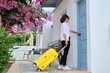 © Valerii Honcharuk - Outdoor, woman traveler with yellow suitcase opening closing door of the house