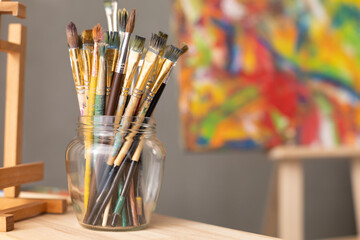 Paint brush in glass jar on wooden table background. Paintbrush and painting as art concept