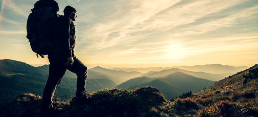 Wall Mural - the man standing with a camping backpack on a rock with a picturesque sunset