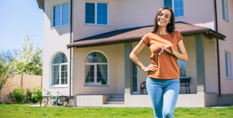 Happy cute woman like an owner with keys in hand in front of big house