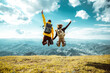 Hikers with backpacks jumping with arms up on top of a mountain - Couple of young happy travelers climbing the peak - Family, travel and adventure concept