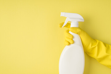 Top view photo of hand in yellow rubber glove using spay detergent white bottle without label on isolated yellow background with blank space