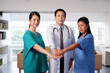 © cocorattanakorn - Asian chief physician man is holding hand with surgeon doctor women wears blue and green surgical gown together. Smiling Medical team in meeting room at hospital.