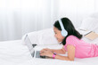 © Rakchanok - Adorable Asian girl concentrate online education class on laptop, kids lie down on bed watching game or social media connect to friends, smart school girl study e-learning using headphone technology