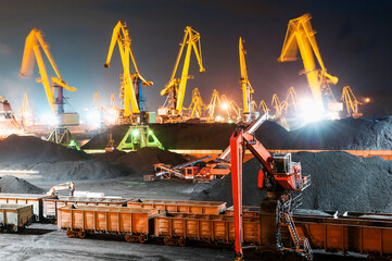 Coal terminal at the seaport at night.
Mountains of coal, Belt conveyors, Portal and hydraulic cranes, industrial wagons.