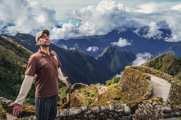 Wall Mural - High angle view of a man breathing the air with eyes closed and open arms, with huge valley behind, on Phuyupatamarca ruins. Inca trail to Machu Picchu in Peru. South America