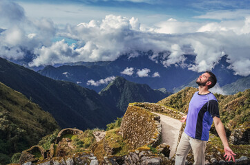 Wall Mural - High angle view of a man breathing the air with eyes closed and open arms, with huge valley behind, on Phuyupatamarca ruins. Inca trail to Machu Picchu in Peru. South America