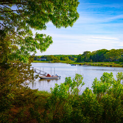 Wall Mural - Tranquil harbor landscape in Falmouth on Cape Cod. Moored Boat at private dock surrounded by green forest. Summer idle island seascape in New England.