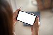 © amnaj - Close-up of a woman hand holding a smartphone horizontally with a blank white screen. Mock up.