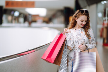 Young woman after shopping with shopping bags walking in the mall. Consumerism, sale, purchases, shopping, lifestyle concept.