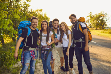 Wall Mural - group of smiling young people friends backpackers standing near road during hiking together on summe