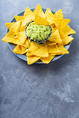 Mexican sauce guacamole with nachos chips in a plate. Bowl of guacamole with nachos chips on a gray background. Copy space. Flat lay