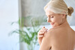 © insta_photos - Back view of naked gorgeous middle aged 50s woman applying moisturizing body lotion after shower. Advertising of bodycare spa procedures, antiage sun protection treatment products concept.