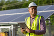 Young asian electrical engineer standing in front of Solar cell panels farm. He using tablet to checking the system. Solar generator power concept.