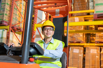 Forklift driver asian man in safety jumpsuit uniform with yellow hardhat at warehouse. Worker male senior looking at camera and smiling in forklift loader work