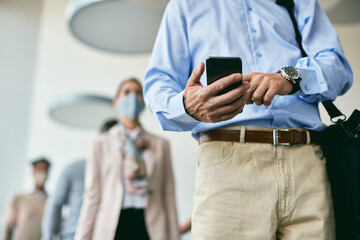 Close-up of businessman text messaging on cell phone while waiting in line due to coronavirus pandemic.