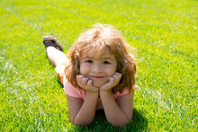 Close Up Portrait Of A Cute Child Laying In Grass In Summer Nature Park.