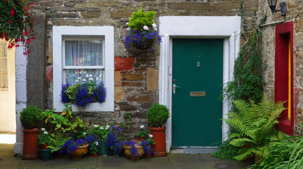  Picturesque facade of a traditional stone house with ornate colored green door and white window. With many pots and flowers in front. kirkwall, scotland