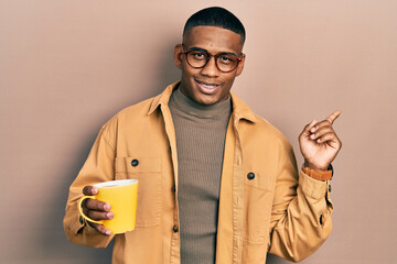 Wall Mural - Young black man wearing glasses and drinking a cup of coffee smiling happy pointing with hand and finger to the side