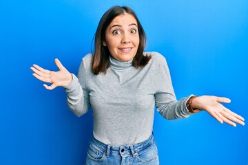 Sticker - Young beautiful woman wearing casual turtleneck sweater clueless and confused expression with arms and hands raised. doubt concept.