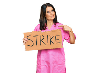 Canvas Print - Middle age brunette doctor woman holding strike banner cardboard pointing finger to one self smiling happy and proud