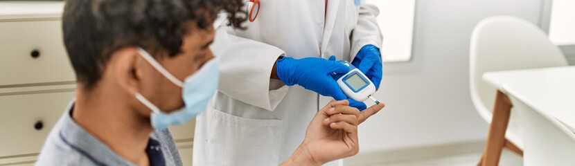 Young latin doctor woman wearing medical mask measuring gluscose at examination room.