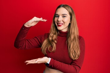 Canvas Print - Young blonde woman wearing turtleneck sweater gesturing with hands showing big and large size sign, measure symbol. smiling looking at the camera. measuring concept.