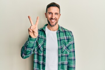 Handsome man with beard wearing casual clothes showing and pointing up with fingers number two while smiling confident and happy.