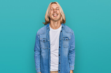 Sticker - Caucasian man with blond long hair wearing casual denim jacket sticking tongue out happy with funny expression. emotion concept.