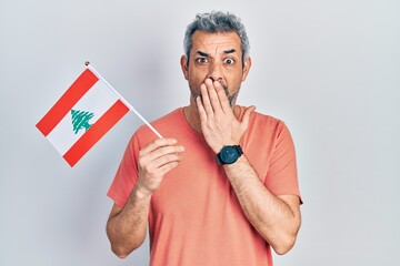 Poster - Handsome middle age man with grey hair holding lebanon flag covering mouth with hand, shocked and afraid for mistake. surprised expression