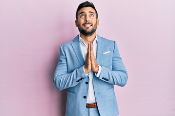 Wall Mural - Young hispanic businessman wearing business jacket begging and praying with hands together with hope expression on face very emotional and worried. begging.