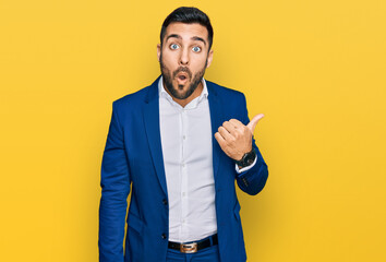 Canvas Print - Young hispanic man wearing business jacket surprised pointing with hand finger to the side, open mouth amazed expression.