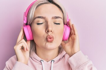 Poster - Young blonde girl listening to music using headphones looking at the camera blowing a kiss being lovely and sexy. love expression.