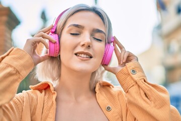 Young blonde girl listening to music using headphones at the city.