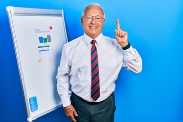 Wall Mural - Senior man with grey hair standing by business blackboard with a big smile on face, pointing with hand finger to the side looking at the camera.