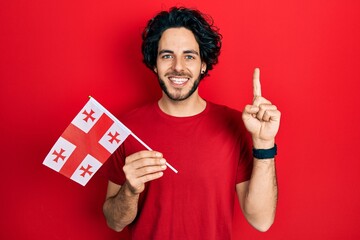 Sticker - Handsome hispanic man holding georgia flag smiling with an idea or question pointing finger with happy face, number one