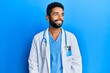 © Krakenimages.com - Handsome hispanic man with beard wearing doctor uniform and stethoscope looking to side, relax profile pose with natural face and confident smile.