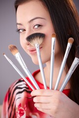 Canvas Print - Beautiful young woman holding make-up brushes, looking at camera, smiling.