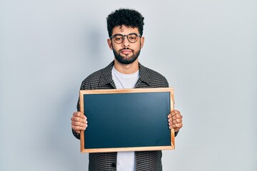 Sticker - Young arab man with beard holding blackboard relaxed with serious expression on face. simple and natural looking at the camera.