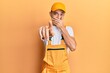 © Krakenimages.com - Hispanic young man wearing handyman uniform laughing at you, pointing finger to the camera with hand over mouth, shame expression