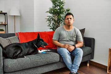 Canvas Print - Young latin man and dog sitting on the sofa at home looking at the camera blowing a kiss on air being lovely and sexy. love expression.